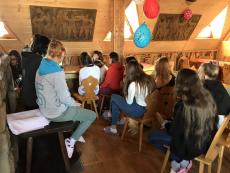 Dzieci słuchają wykładu w drewnianej izbie - widok z tyłu 
