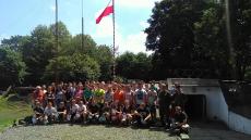 Duża grupa dzieci i opiekunów pozuje do zdjęcia na tle drzew i flagi Polski.jpg