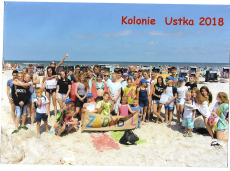 Grupowe zdjęcie dzieci i opiekunów na tle morza na słonecznej plaży.png