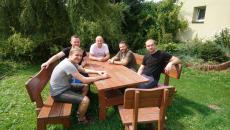Na zdjęciu widać grupę mężczyzn siedzących przy drewnianym stoliku w ogródku - pracownicy - wolontariusze z firmy Firmy Hemmersbach jpg