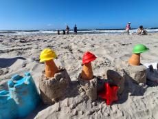 zdjecie-przedstawia-budowle-z-piasku-na-tle-wychowankow-wchodzacych-do-morza.jpg