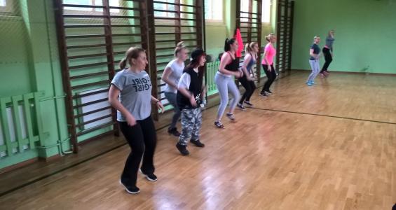 Grupa dzieci i wychowawców trenujących taniec "Zumba" na tle drabinek na sali gimnastycznej.jpg