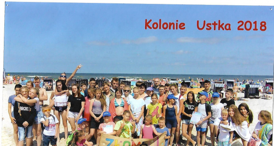 Grupowe zdjęcie dzieci i opiekunów na tle morza na słonecznej plaży.png