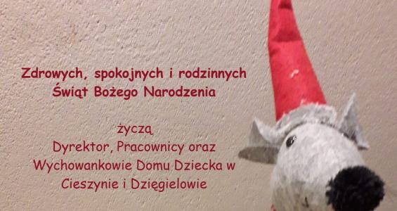 Kartka na której po lewej stronie znajduje się stroik świąteczny a po prawej pluszowy piesek w czerwonych spodniach i w czapeczce Świętego Mikołaja.jpg