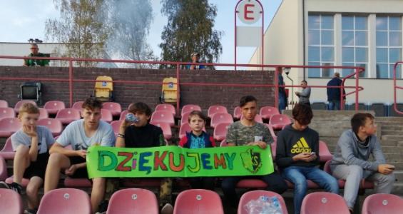 Pusty stadion piłkarskich - siedzenie w dwóch ostatnich rzędach siedzi grupa dzieci z kolorowym napisem dziękujemy na zielonej kartce.jpg